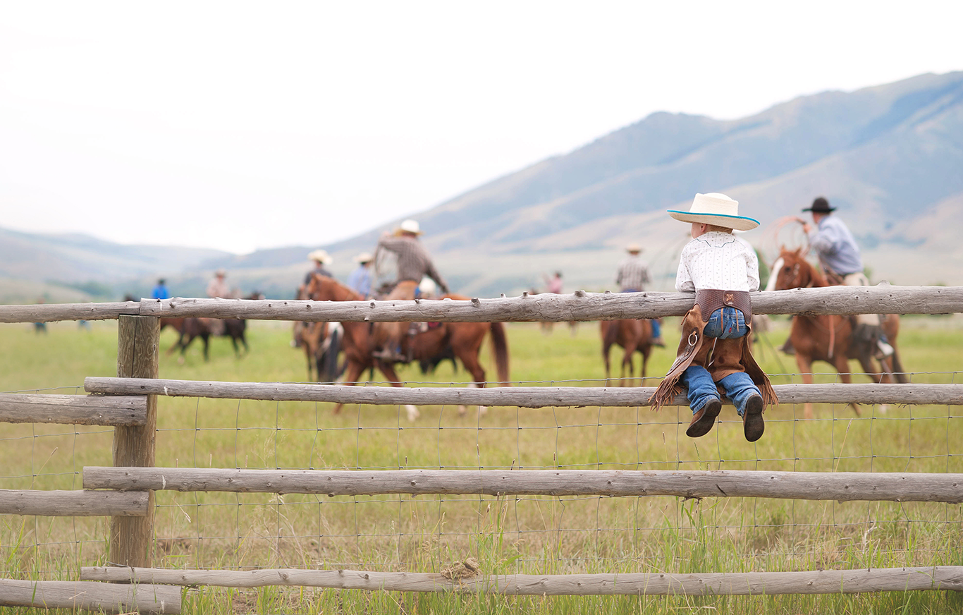 Child dressed in cowboy clothing sitting on a fence